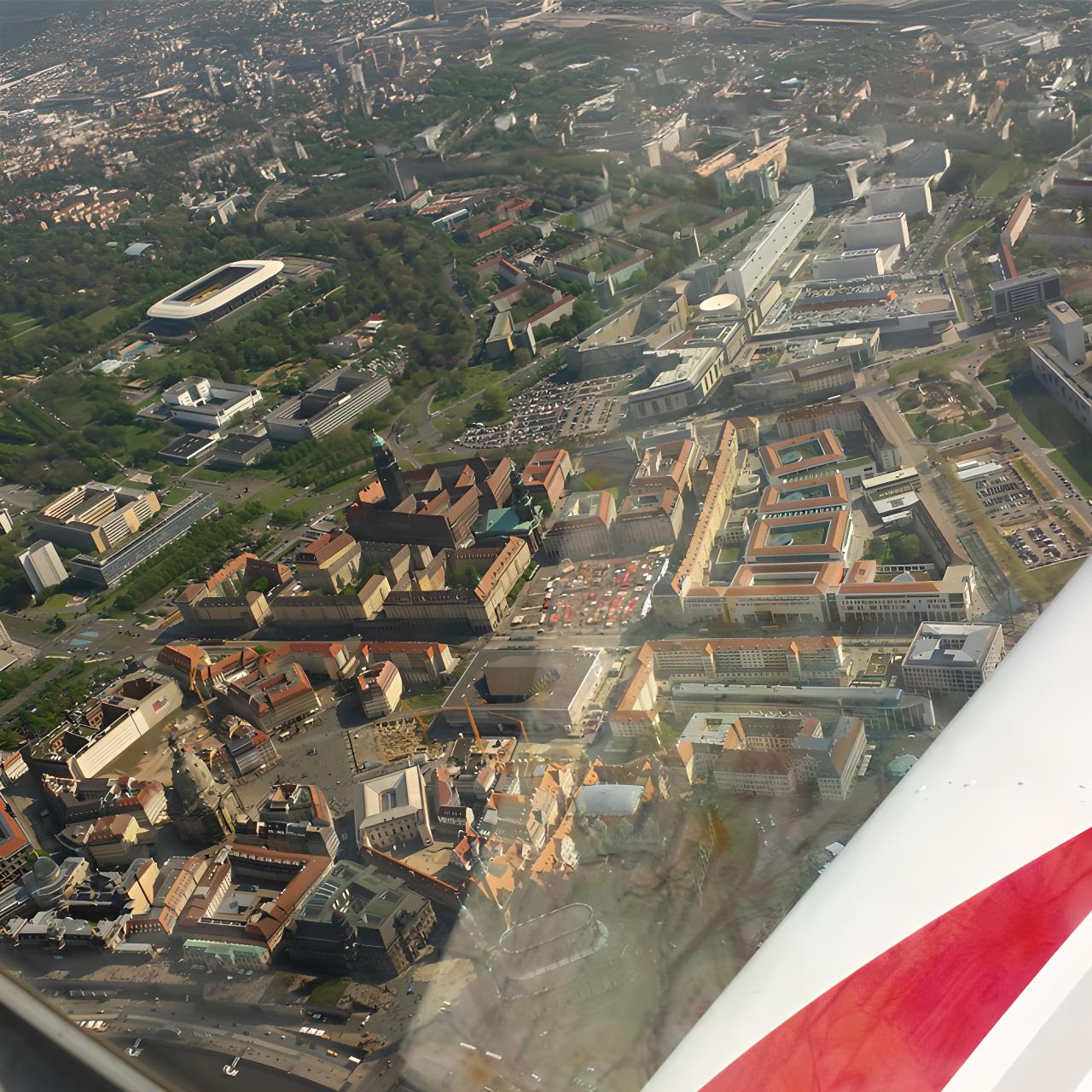 Schrägluftaufnahme einer Stadt mit historischen und modernen Gebäuden, aufgenommen aus einem Flugzeug mit Blick auf die Tragfläche.