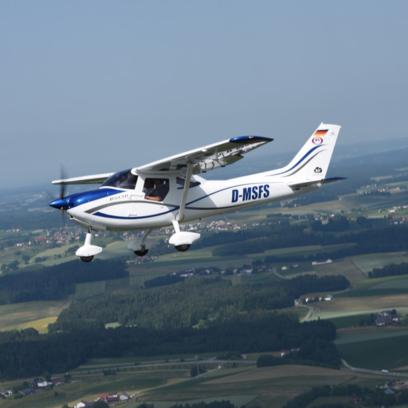 Leichtflugzeug mit der Kennung D-MSFS im Flug über einer ländlichen Landschaft bei klarem Himmel.